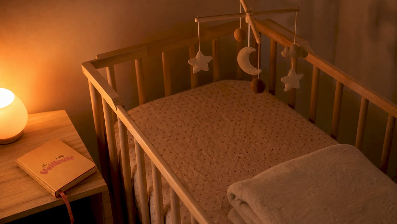 Dans la chambre de bébé, une veilleuse rouge diffuse une lumière douce et rassurante, créant une atmosphère paisible propice au sommeil.