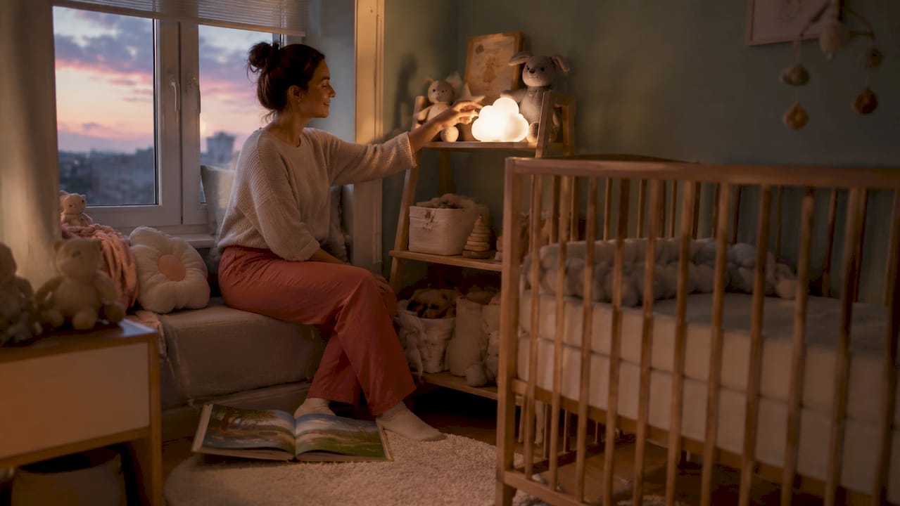 Une maman règle délicatement la veilleuse douce à côté du lit de son bébé pour créer une ambiance rassurante.