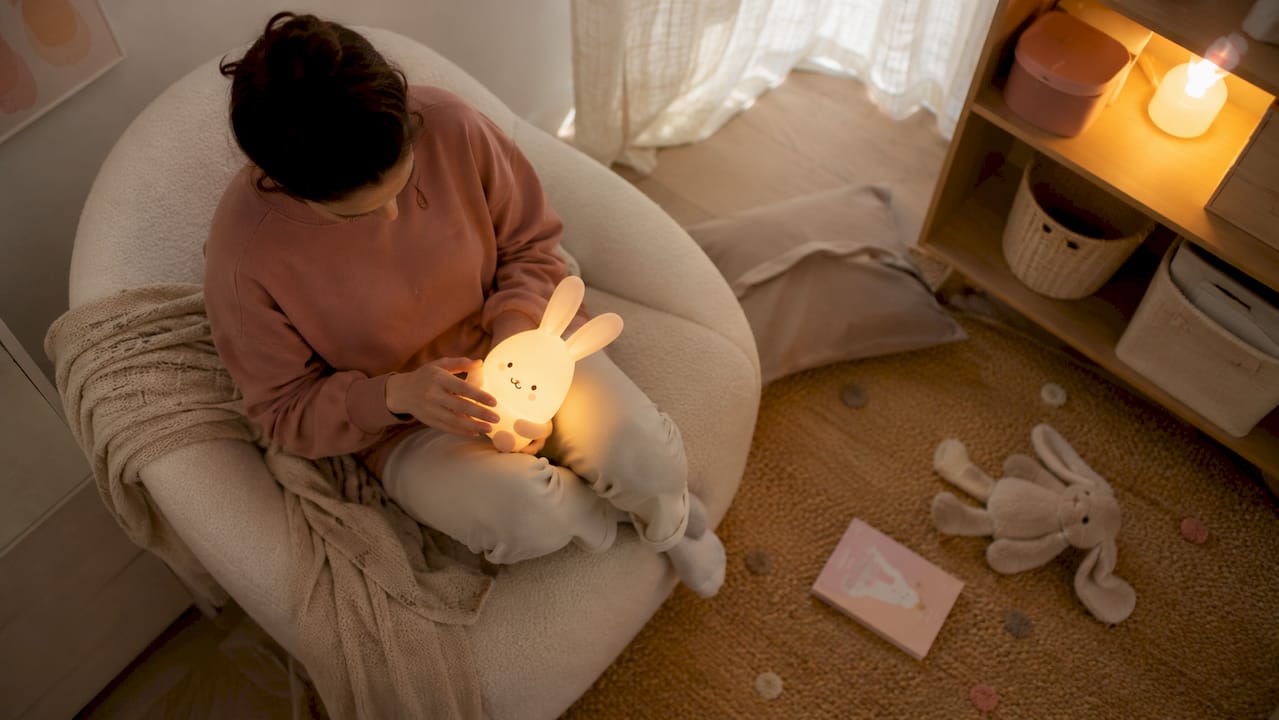 Un parent tient un doudou lumineux pour rassurer son enfant dans la chambre, créant une ambiance douce et réconfortante avant le coucher.