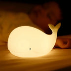 Veilleuse baleine bébé posée près d’un enfant endormi, offrant une lumière réconfortante pour un sommeil paisible et sécurisé.