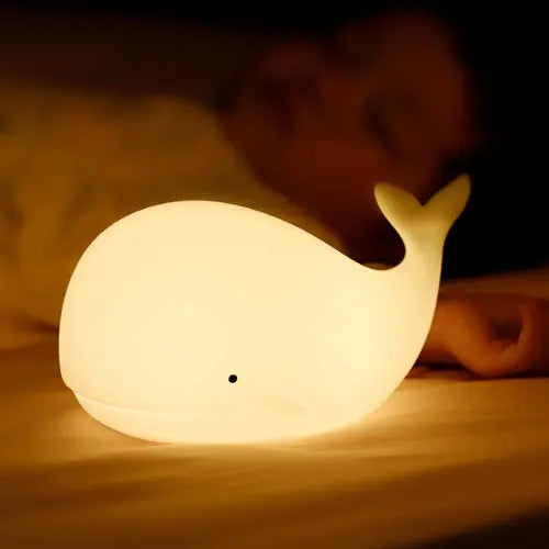 Veilleuse baleine bébé posée près d’un enfant endormi, offrant une lumière réconfortante pour un sommeil paisible et sécurisé.